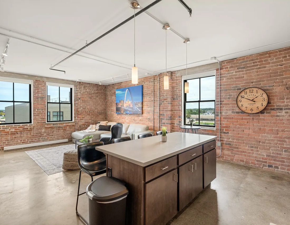 A spacious Harbach Lofts kitchen and living area with original brick, factory windows, and skyline art